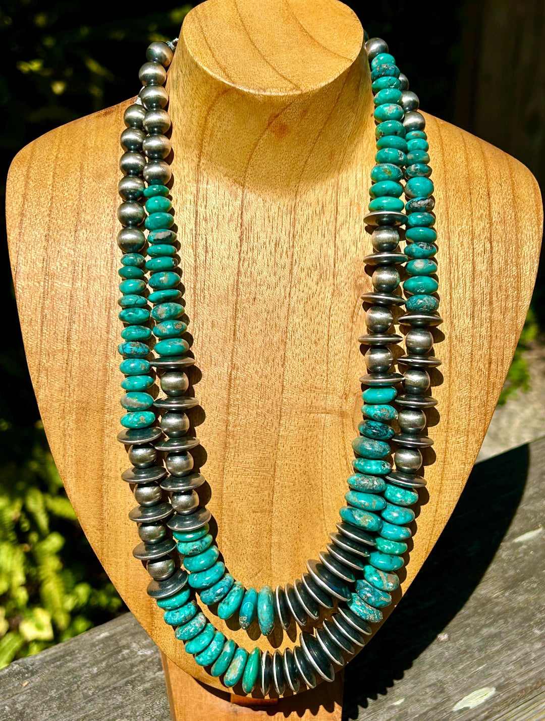 May include: A turquoise and silver necklace with two strands of beads. The turquoise beads are a bright, vibrant blue-green color. The silver beads are round and have a smooth, polished finish. The necklace is displayed on a wooden mannequin.